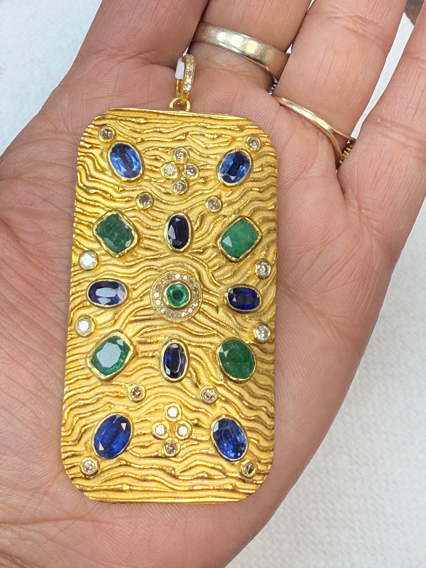 A gold-colored pendant with diamond and gemstone pave charms, held in a person's hand.