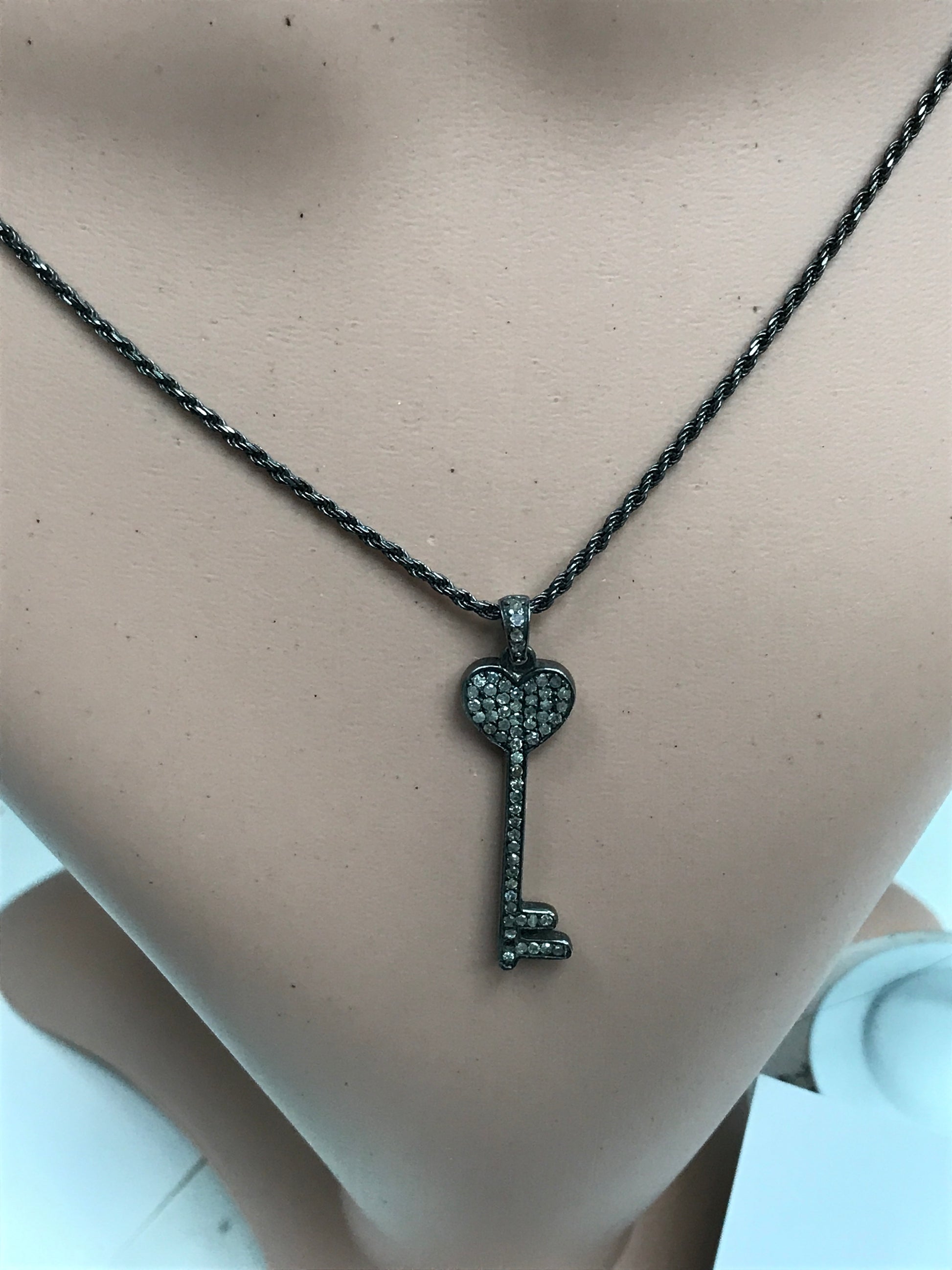 A key-shaped diamond pendant on a silver necklace displayed on a mannequin bust.